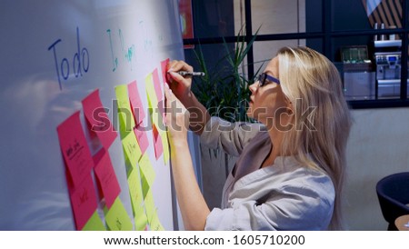 Project management agile methodology, concept. A young blonde woman in glasses, gluing colored sticky notes on a magnetic Board.