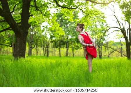 Young sports girl in a red dress practices yoga in a quiet green forest. Meditation and oneness with nature.