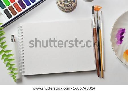 Notepad with watercolor paper and brush on the desktop