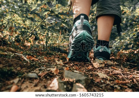 Muddy boots of hiker on forest trail. Traveler feet are stepping on the ground with fallen leaves. Close up of the sole of dirty shoes. Adventure and hiking concept outdoor. Hipster lifestyle Royalty-Free Stock Photo #1605743215