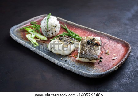 Gourmet fried Japanese skrei cod fish filet with glasswort and furikake onigiri as closeup on a modern design plate 