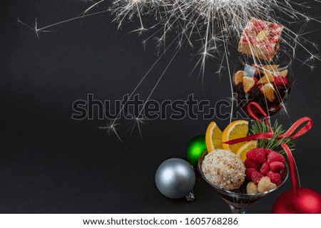 Holiday sweets and fruits in a glass and christmas toys on a black background with sparkler