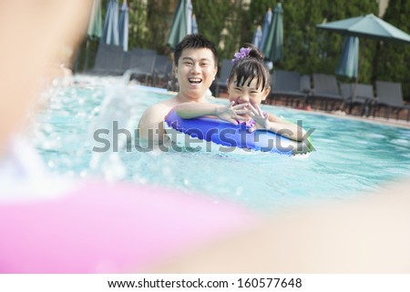 Young smiling family splashing and playing in pool