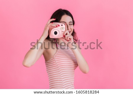 A young girl in a pink striped dress holds a camera in her hands