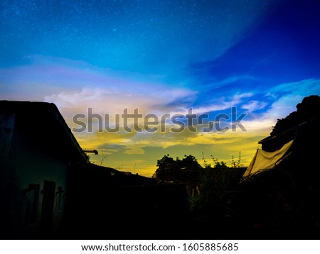 Natural Sunset in evening rise field silhouette at India. Bright Dramatic Sky And Dark houses. Countryside Landscape Under Scenic Colorful Sky At Sunset. Sun Over Skyline, Horizon. Warm Colors.