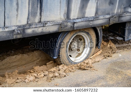 Photo of a heavy truck stuck in mud and skidding in place on a cloudy day.