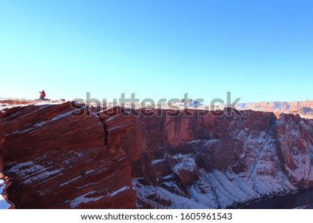 Distant view of a man taking picture at Horseshoe bend, red sandstone covered with snow