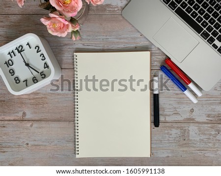 Image of laptop, light orange roses, red, blue, black marker pen, mechanical pencil, drawing note pad, white clock show 5 am for early on wooden table background. Concept of business copy space.