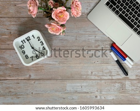 Image of laptop, light orange roses, red, blue, black marker pen, drawing note pad, white clock show 5 am for early on wooden table background. Concept of business copy space.