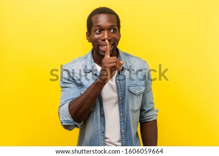 Please, keep silence. Portrait of cheerful handsome man in denim casual shirt gesturing to be quiet with fingers on his lips, asking for secrecy. indoor studio shot isolated on yellow background