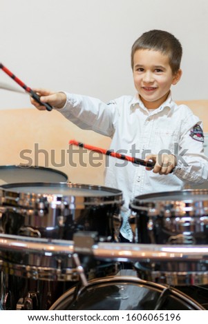 Boy drumming. boy in a white shirt plays the drums. A boy in a white shirt is drumming. Vertical photo
