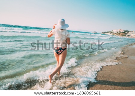 Young Caucasian Lady Woman In Summer Hat Runs Along The Seashore Sea Beach. Vacation On Sea Ocean Beach.