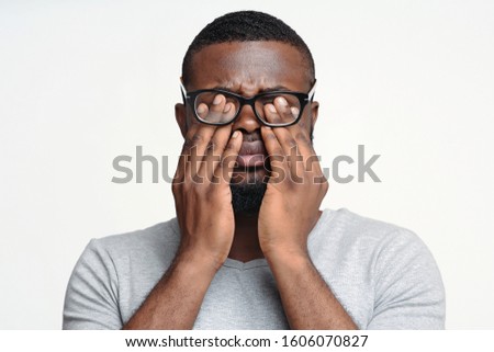 Tired eyes concept. Black man in glasses rubbing his eyes, white studio background Royalty-Free Stock Photo #1606070827