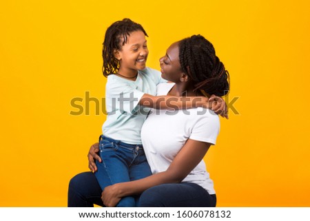 Happy Loving Family. Overjoyed black daughter sitting on mother's lap looking at each other over yellow background