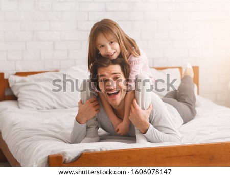 Father and daughter spending weekend together at home. Little girl riding fathers back in bedroom, free space
