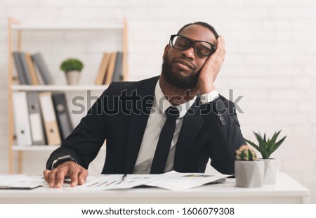 Tired young black businessman in glasses having nap on workplace, overworking, copy space