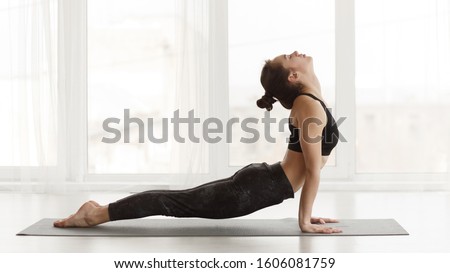 Fit woman making cobra pose on yoga mat, exercising in studio over panoramic window Royalty-Free Stock Photo #1606081759