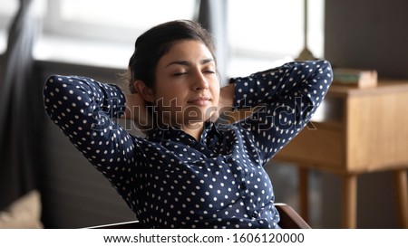 Calm relaxed indian lady rest at home office sit on chair with eyes shut hold hands behind head, ethnic woman relax after work feel peace of mind dream think do exercises for neck back muscles relief Royalty-Free Stock Photo #1606120000