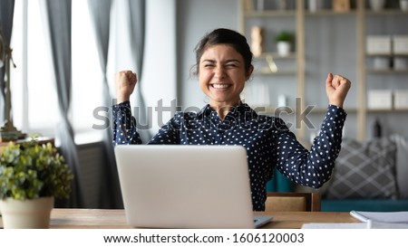 Euphoric young indian girl student winner celebrate victory triumph sit at home desk with laptop computer win online fortune feel excited get new job opportunity good exam result great news concept Royalty-Free Stock Photo #1606120003