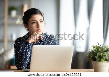 Serious thoughtful pensive young indian ethnic woman student sit at home office desk with laptop thinking of inspiration solution lost in thoughts dreaming looking away search creative ideas concept Royalty-Free Stock Photo #1606120021