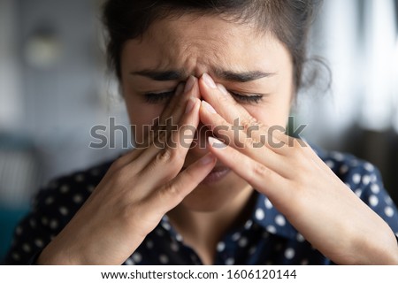 Sick frustrated sad young indian woman in pain cope with headache, eye strain emotional mental stress cry feel anxiety pressure panic attack touching nose bridge, face close up view, migraine concept Royalty-Free Stock Photo #1606120144