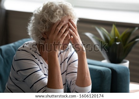 Close up 70s elderly woman sitting on sofa feels desperate crying covered face with hands, senile sickness need help, mental disorder or dementia, does not see way out difficult life situation concept Royalty-Free Stock Photo #1606120174