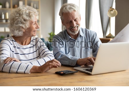Elderly couple sitting at table using laptop and online banking feels satisfied checking utility bills or financial statement papers, easy access, reading good news received letter from bank concept Royalty-Free Stock Photo #1606120369