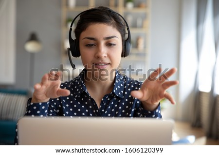 Indian young business woman student teacher tutor wear wireless headset video conference calling on laptop computer talk by webcam learn teach in online chat, distance webinar online teaching concept Royalty-Free Stock Photo #1606120399