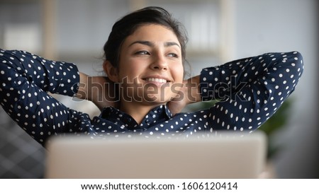 Happy satisfied indian woman rest at home office sit with laptop hold hands behind head, dreamy young lady relax finished work feel peace of mind look away dream think of future success concept Royalty-Free Stock Photo #1606120414