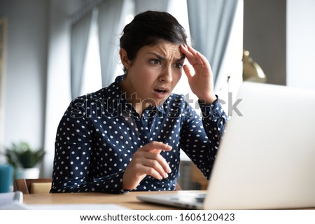Shocked afraid worried young indian girl look at laptop computer screen terrified read bullying social media message feel bad surprise stress panic about stuck computer problem concept at home office Royalty-Free Stock Photo #1606120423