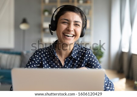 Cheerful indian woman wear headset laugh using laptop video stream conference call teach online, happy ethnic girl student gamer tutor have fun watch webinar web cam education entertainment concept Royalty-Free Stock Photo #1606120429