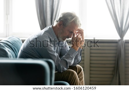 Side view in living room seated on couch hunched old 50s male hold hands near face looking desperate and lonely feels worried. Concept of illness and diagnosis, older generation humans life troubles Royalty-Free Stock Photo #1606120459