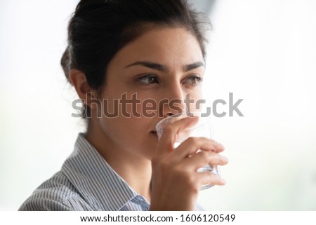 Attractive thirsty young indian woman hold glass drinking fresh mineral pure water, healthy lady hydrate thirst keep healthcare hydration diet nutrition weightloss balance concept, face close up view