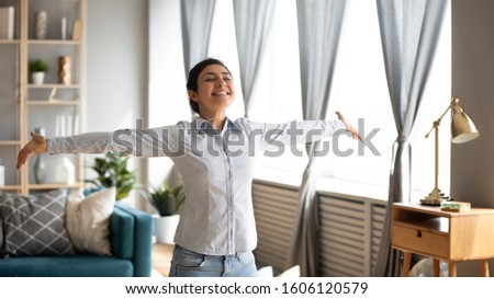 Excited independent young indian woman housewife first time home owner stand in modern living room interior with arms outstretched enjoy free lifestyle freedom wellbeing dance alone in own apartment Royalty-Free Stock Photo #1606120579