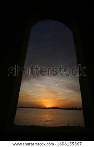 Panoramic sunset over Dakar city, Capital of Senegal, West Africa. Cloudy colorful sky in the background. Atlantic ocean at the foreground. Arched frame. Seascape picture taken from Goree Island.