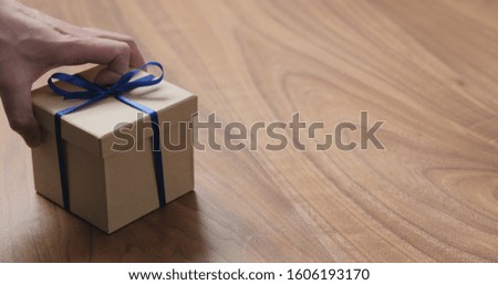 man hand place eco friendly paper gift box with blue ribbon on walnut table with copy space