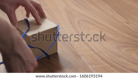 man hands opens eco friendly paper gift box with blue ribbon on walnut table with copy space