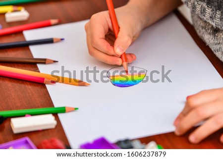 A girl draws a heart with colored pencils on a white sheet among children's toys.