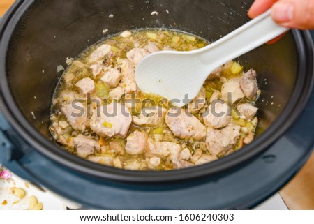 Woman stirs the stew with a white spoon in a slow cooker.