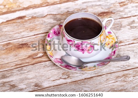 White porcelain Cup with a delicate pattern of pink and yellow rose buds with instant coffee with a spoon and two pieces of sugar on a saucer on a wooden background.
