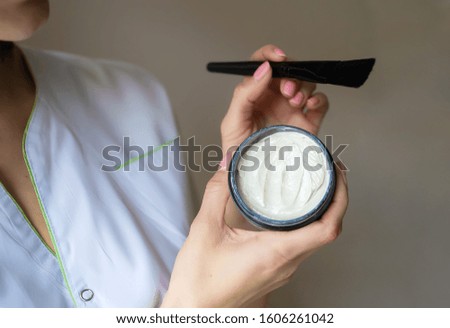 Closeup photo of cosmetologist's hands holding brush and peeling cream in small box