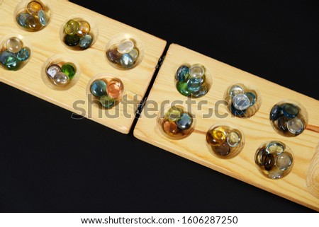 wooden mangala game, mangala game board and glass marbles, on black background