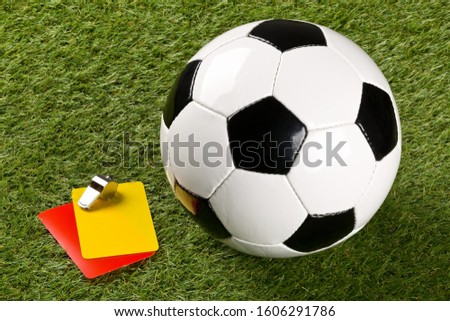 Soccer ball with referee yellow and red cards and chrome whistle on grass background - penalty, foul or sports concept, selective focus