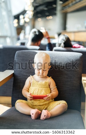 One-year-old child sits in a chair and uses a smartphone to watch cartoons. Technology and Children.