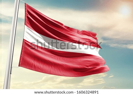 Latvia national flag cloth fabric waving on the sky with beautiful sun light