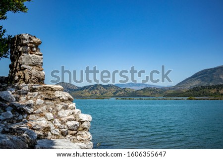 Sunny spring day view of salt lagoon lake, valley and mountain in the national park of Butrint in Albania, Europe. Fortress stone ruined wall in the foreground.