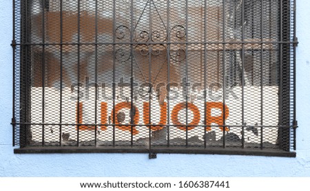 Shabby LIQUOR store sign behind rusty window security grate.