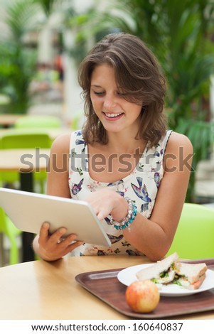 Young woman using tablet PC while having meal in the cafeteria