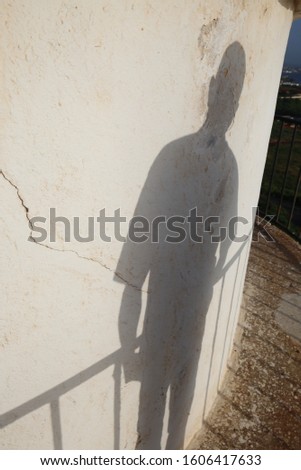 Human shadows on a white curved surface. Standing silhouette beside a metallic barrier. 