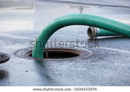 the green thick hose from a sewer pit, pumping sewage or sewage from collector in city. water drainage. Sewer manhole with an open manhole cover and large corrugated suction hoses for waste Royalty-Free Stock Photo #1606450696